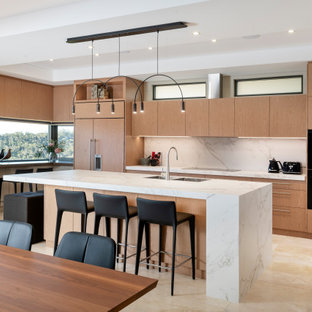 Large contemporary l-shaped open plan kitchen in Perth with a double-bowl sink, recessed-panel cabinets, light wood cabinets, white splashback, black appliances, travertine floors, with island, beige floor and white benchtop.