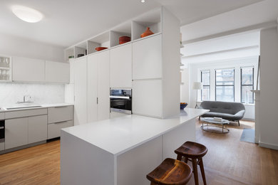 Inspiration for a mid-sized modern u-shaped light wood floor kitchen pantry remodel in New York with an undermount sink, flat-panel cabinets, white cabinets, solid surface countertops, multicolored backsplash, stone slab backsplash, paneled appliances and an island