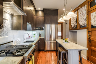 Mid-sized elegant l-shaped medium tone wood floor and brown floor enclosed kitchen photo in Chicago with an undermount sink, shaker cabinets, gray cabinets, granite countertops, white backsplash, subway tile backsplash, stainless steel appliances and an island