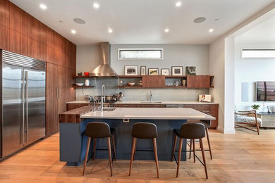 Design ideas for a medium sized contemporary l-shaped open plan kitchen in San Francisco with a submerged sink, flat-panel cabinets, dark wood cabinets, composite countertops, grey splashback, porcelain splashback, stainless steel appliances, light hardwood flooring and an island.