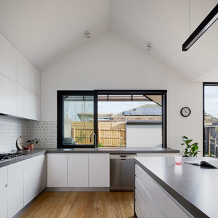 Large contemporary u-shaped open plan kitchen in Melbourne with flat-panel cabinets, white cabinets, quartz benchtops, ceramic splashback, stainless steel appliances, with island, grey benchtop, a drop-in sink, multi-coloured splashback, medium hardwood floors and beige floor.