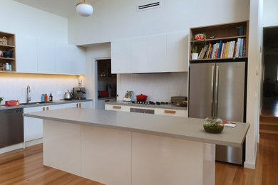 Idéer för att renovera ett mellanstort funkis grå grått kök, med en undermonterad diskho, släta luckor, vita skåp, bänkskiva i kvarts, vitt stänkskydd, stänkskydd i porslinskakel, rostfria vitvaror, mellanmörkt trägolv, en köksö och brunt golv