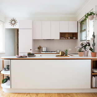 Photo of a small midcentury u-shaped open plan kitchen in Adelaide with flat-panel cabinets, laminate benchtops, white splashback, ceramic splashback, white appliances and light hardwood floors.