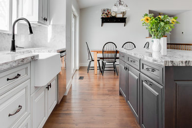 Kitchen - mid-sized transitional galley medium tone wood floor and brown floor kitchen idea in Salt Lake City with a farmhouse sink, raised-panel cabinets, gray cabinets, granite countertops, white backsplash, marble backsplash, paneled appliances and an island