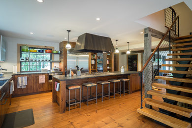 Kitchen - mid-sized rustic l-shaped medium tone wood floor and brown floor kitchen idea in Philadelphia with a farmhouse sink, medium tone wood cabinets, soapstone countertops, white backsplash, glass tile backsplash, stainless steel appliances, an island and flat-panel cabinets
