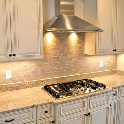 Inspiration for a mid-sized transitional u-shaped medium tone wood floor enclosed kitchen remodel in Boston with an undermount sink, raised-panel cabinets, white cabinets, granite countertops, beige backsplash, stone tile backsplash, stainless steel appliances and a peninsula