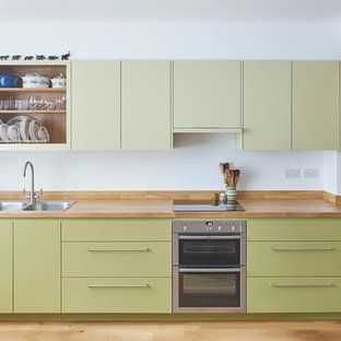 Inspiration for a mid-sized eclectic single-wall open plan kitchen in London with a double-bowl sink, flat-panel cabinets, green cabinets, wood benchtops, panelled appliances, light hardwood floors and no island.