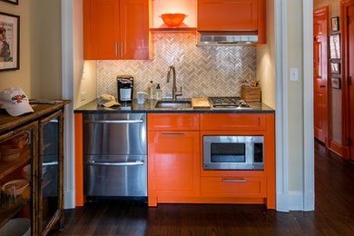 Example of a small eclectic single-wall dark wood floor and brown floor open concept kitchen design in New York with an undermount sink, shaker cabinets, orange cabinets, granite countertops, gray backsplash, marble backsplash, stainless steel appliances, no island and gray countertops