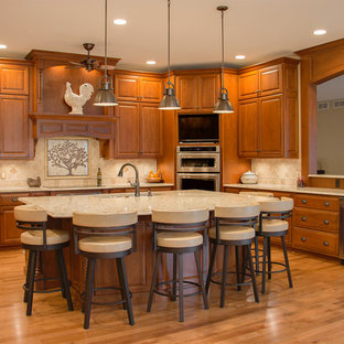 Réalisation d'une grand cuisine américaine tradition en U avec un évier encastré, un placard avec porte à panneau surélevé, des portes de placard en bois brun, un électroménager en acier inoxydable, un sol en bois clair, un îlot central, un plan de travail en quartz modifié, une crédence beige et une crédence en carrelage de pierre.