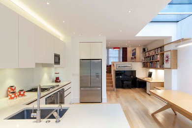 This is an example of a small contemporary u-shaped kitchen/diner in London with a submerged sink, flat-panel cabinets, white cabinets, quartz worktops, white splashback, glass sheet splashback, stainless steel appliances, medium hardwood flooring and a breakfast bar.