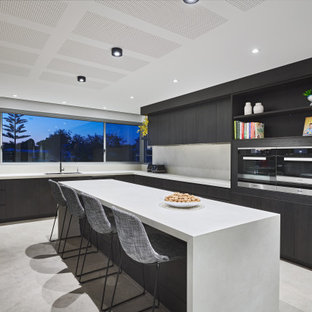 Photo of a large contemporary l-shaped eat-in kitchen in Perth with a double-bowl sink, flat-panel cabinets, grey cabinets, solid surface benchtops, window splashback, black appliances, porcelain floors, with island, grey floor and grey benchtop.