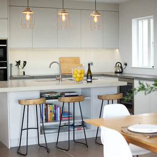 Design ideas for a medium sized contemporary galley kitchen/diner in Channel Islands with flat-panel cabinets, grey cabinets, concrete worktops, beige splashback, glass sheet splashback, ceramic flooring, an island, grey floors, a submerged sink, black appliances and grey worktops.