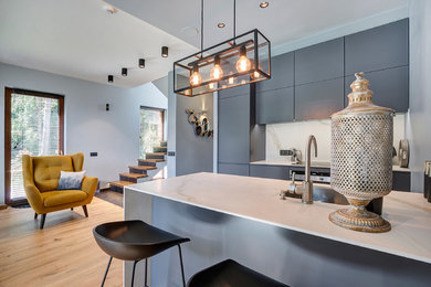 This is an example of a small contemporary galley open plan kitchen in Other with a submerged sink, flat-panel cabinets, grey cabinets, marble worktops, white splashback, marble splashback, stainless steel appliances and black floors.