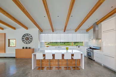 Moderne Küche in L-Form mit Unterbauwaschbecken, flächenbündigen Schrankfronten, weißen Schränken, Küchenrückwand in Weiß, Elektrogeräten mit Frontblende, Betonboden und Kücheninsel in Vancouver