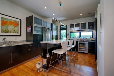 Example of a mid-sized trendy l-shaped medium tone wood floor and brown floor enclosed kitchen design in Columbus with an undermount sink, flat-panel cabinets, black cabinets, granite countertops, stainless steel appliances and an island