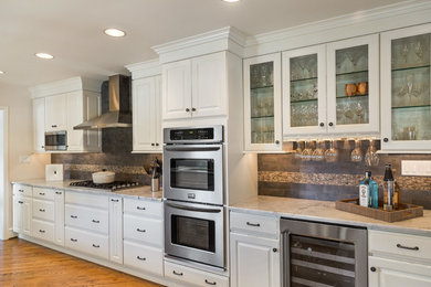 Inredning av ett klassiskt stort kök, med en undermonterad diskho, luckor med upphöjd panel, vita skåp, granitbänkskiva, grått stänkskydd, stänkskydd i porslinskakel, rostfria vitvaror och mellanmörkt trägolv