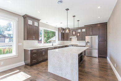Open concept kitchen - large modern l-shaped dark wood floor and brown floor open concept kitchen idea in Vancouver with an undermount sink, brown cabinets, granite countertops, beige backsplash, stainless steel appliances, an island and beige countertops