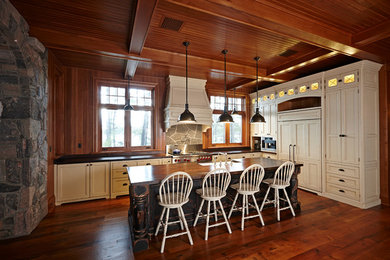 Example of a large mountain style l-shaped medium tone wood floor eat-in kitchen design in Toronto with a farmhouse sink, recessed-panel cabinets, distressed cabinets, wood countertops, paneled appliances and an island