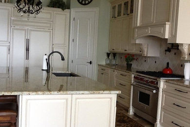 This is an example of a large mediterranean l-shaped open plan kitchen in New Orleans with a submerged sink, raised-panel cabinets, beige cabinets, granite worktops, beige splashback, integrated appliances, travertine flooring and an island.