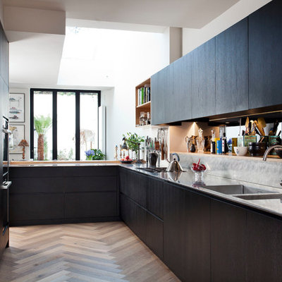 Kitchen - mid-sized contemporary l-shaped medium tone wood floor kitchen idea in Dublin with an integrated sink, flat-panel cabinets, stainless steel countertops, metallic backsplash, a peninsula and black cabinets