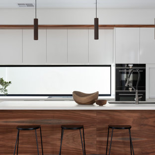 Large contemporary galley kitchen in Perth with an undermount sink, flat-panel cabinets, white cabinets, mirror splashback, panelled appliances, with island, grey floor and white benchtop.