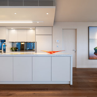 Photo of a contemporary galley eat-in kitchen in Sydney with an undermount sink, flat-panel cabinets, white cabinets, mirror splashback, panelled appliances, medium hardwood floors, with island, brown floor and white benchtop.