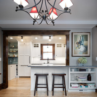 Photo of a mid-sized traditional u-shaped eat-in kitchen in Minneapolis with a farmhouse sink, shaker cabinets, white cabinets, recycled glass benchtops, white splashback, subway tile splashback, panelled appliances, light hardwood floors, a peninsula, brown floor and grey benchtop.