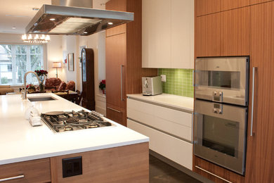バンクーバーにあるラグジュアリーな小さなコンテンポラリースタイルのおしゃれなキッチン (シングルシンク、フラットパネル扉のキャビネット、中間色木目調キャビネット、クオーツストーンカウンター、緑のキッチンパネル、ガラスタイルのキッチンパネル、パネルと同色の調理設備、無垢フローリング、茶色い床、白いキッチンカウンター) の写真