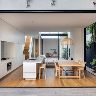 Inspiration for a contemporary galley eat-in kitchen in Los Angeles with an undermount sink, flat-panel cabinets, white cabinets, grey splashback, medium hardwood floors, with island, brown floor and white benchtop.