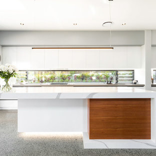 This is an example of a large contemporary galley open plan kitchen in Brisbane with flat-panel cabinets, white cabinets, window splashback, stainless steel appliances, with island, grey floor, white benchtop, a drop-in sink, quartz benchtops and concrete floors.