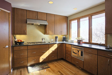 Example of a mid-sized classic l-shaped light wood floor enclosed kitchen design in Seattle with an undermount sink, flat-panel cabinets, medium tone wood cabinets, soapstone countertops, beige backsplash, mosaic tile backsplash, stainless steel appliances and no island