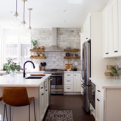 Transitional l-shaped laminate floor and brown floor kitchen photo in Los Angeles with an undermount sink, shaker cabinets, white cabinets, quartz countertops, gray backsplash, marble backsplash, stainless steel appliances and an island
