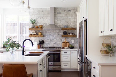 Design ideas for a classic l-shaped kitchen in Los Angeles with a submerged sink, shaker cabinets, white cabinets, engineered stone countertops, grey splashback, marble splashback, stainless steel appliances, laminate floors, an island and brown floors.
