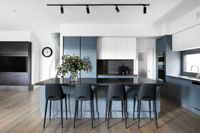 Inspiration for a contemporary l-shaped open plan kitchen in Melbourne with a submerged sink, flat-panel cabinets, grey cabinets, black splashback, integrated appliances, medium hardwood flooring, an island, brown floors and black worktops.
