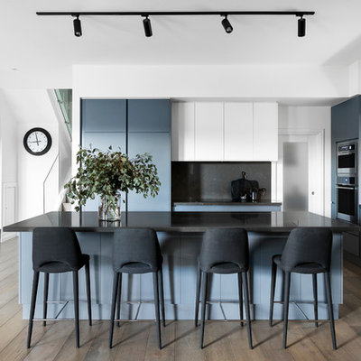 Open concept kitchen - contemporary l-shaped medium tone wood floor and brown floor open concept kitchen idea in Melbourne with an undermount sink, flat-panel cabinets, gray cabinets, black backsplash, paneled appliances, an island and black countertops