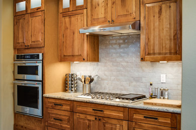 Example of a mid-sized classic galley medium tone wood floor and brown floor open concept kitchen design in San Diego with a farmhouse sink, raised-panel cabinets, medium tone wood cabinets, granite countertops, beige backsplash, subway tile backsplash, stainless steel appliances and an island