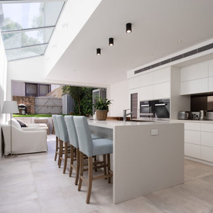 This is an example of a contemporary l-shaped kitchen in Sydney with flat-panel cabinets, white cabinets, stainless steel appliances, with island, grey floor and grey benchtop.