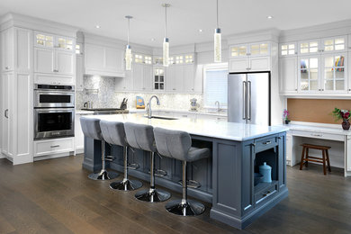 Large traditional l-shaped kitchen/diner in Toronto with a submerged sink, shaker cabinets, white cabinets, engineered stone countertops, multi-coloured splashback, mosaic tiled splashback, stainless steel appliances, medium hardwood flooring and an island.