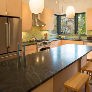 Inspiration for a large contemporary l-shaped eat-in kitchen in New York with medium hardwood floors, with island, a drop-in sink, flat-panel cabinets, light wood cabinets, limestone benchtops, green splashback, glass tile splashback and stainless steel appliances.