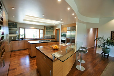 Eat-in kitchen - large contemporary l-shaped medium tone wood floor eat-in kitchen idea in Other with an undermount sink, flat-panel cabinets, medium tone wood cabinets, wood countertops, green backsplash, glass sheet backsplash, stainless steel appliances and two islands