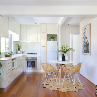 Photo of a contemporary l-shaped eat-in kitchen in Sydney with an undermount sink, flat-panel cabinets, white cabinets, white splashback, white appliances, medium hardwood floors, no island, brown floor and white benchtop.