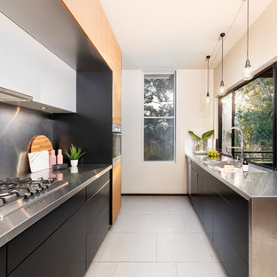 This is an example of a contemporary kitchen in Other with an integrated sink, flat-panel cabinets, black cabinets, stainless steel benchtops, metallic splashback, no island, white floor and grey benchtop.