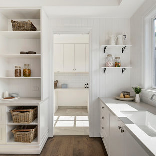 Beach style l-shaped kitchen in Melbourne with an undermount sink, shaker cabinets, white cabinets, white splashback, medium hardwood floors, brown floor and grey benchtop.