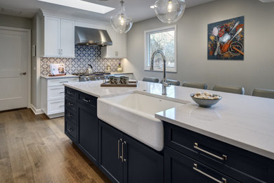 Example of a mid-sized classic l-shaped medium tone wood floor and brown floor eat-in kitchen design in Chicago with a farmhouse sink, raised-panel cabinets, white cabinets, quartz countertops, multicolored backsplash, ceramic backsplash, stainless steel appliances, an island and white countertops