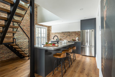 Medium sized urban l-shaped kitchen in Toronto with a submerged sink, flat-panel cabinets, engineered stone countertops, brick splashback, stainless steel appliances, medium hardwood flooring, an island, brown floors, grey worktops and grey cabinets.