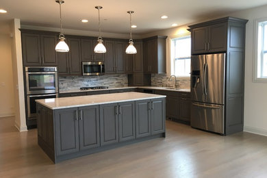 Transitional l-shaped light wood floor and gray floor open concept kitchen photo in Chicago with a double-bowl sink, raised-panel cabinets, gray cabinets, quartz countertops, gray backsplash, stone tile backsplash, stainless steel appliances and an island