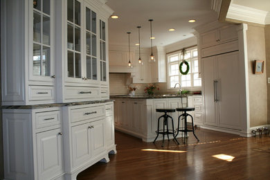 Klassisk inredning av ett kök, med mellanmörkt trägolv, en köksö, vita skåp, granitbänkskiva, beige stänkskydd, stänkskydd i tunnelbanekakel, en rustik diskho och rostfria vitvaror