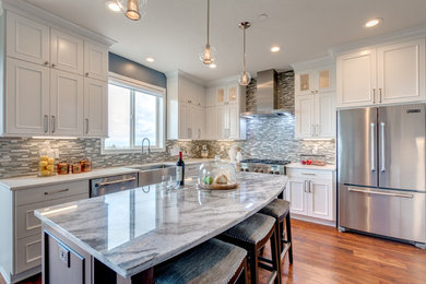 Mid-sized transitional medium tone wood floor open concept kitchen photo in Portland with a farmhouse sink, raised-panel cabinets, white cabinets, quartzite countertops, gray backsplash, matchstick tile backsplash, stainless steel appliances and an island