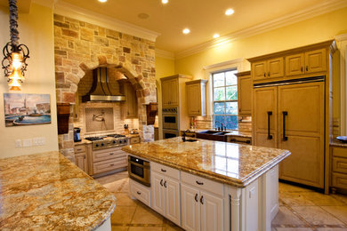 Example of a large tuscan u-shaped porcelain tile and beige floor open concept kitchen design in Dallas with a farmhouse sink, raised-panel cabinets, distressed cabinets, granite countertops, beige backsplash, porcelain backsplash, paneled appliances, an island and brown countertops
