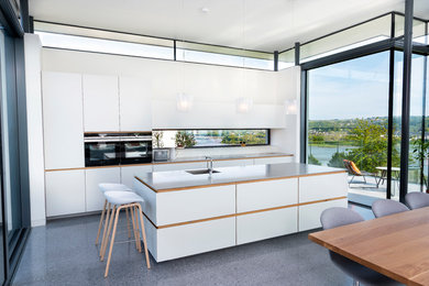This is an example of a medium sized contemporary kitchen/diner in Cork with a single-bowl sink, flat-panel cabinets, white cabinets, window splashback, black appliances, concrete flooring, an island and grey floors.
